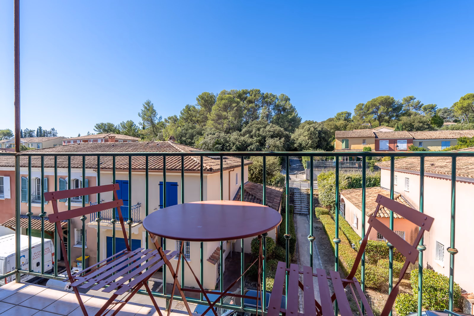 Balcon avec table de bistrot donnant sur les résidences aux façades pastel du centre du village de Saint-Clément-de-Rivière