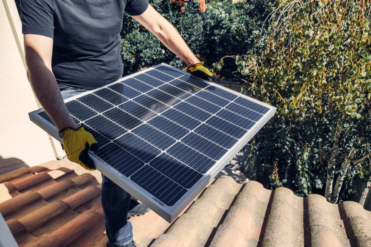 Installateur portant un panneau photovoltaïque sur une toiture en tuiles canal, dans l'Hérault