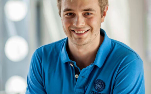 Homme souriant en polo bleu Franklin Marshall portrait en intérieur avec fond flou.