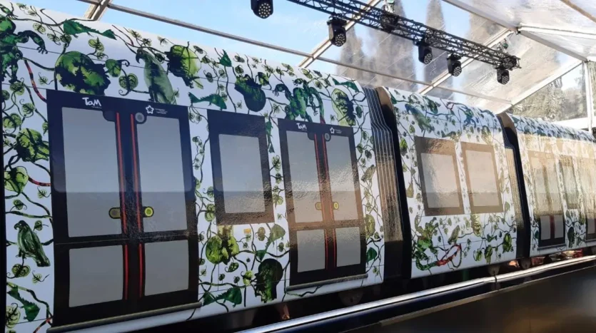 Wagon de métro peint avec motif de feuilles vertes sous une structure en verre avec éclairage.