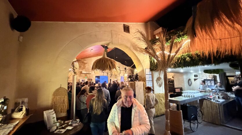 Salle intérieure animée avec arc en pierre, décorations en paille et bar à droite.