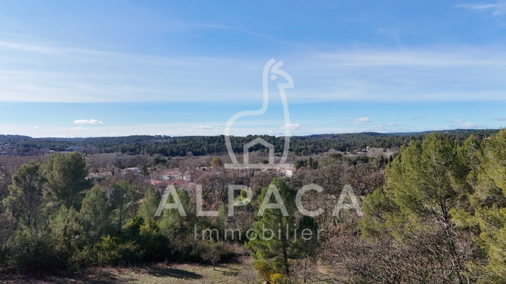 Vue panoramique d'une zone boisée avec maisons dispersées sous un ciel partiellement nuageux.